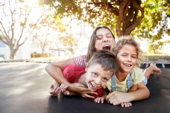Portrait Of Siblings With Teenage Sister Playing On Outdoor Trampoline In Garden