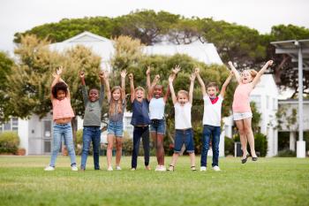 Group Of Excited Elementary School Pupils Standing On Playing Field At Break Time With Arms Raised