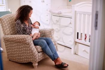 Loving Mother Sitting In Chair Cuddling Baby Son In Nursery At Home