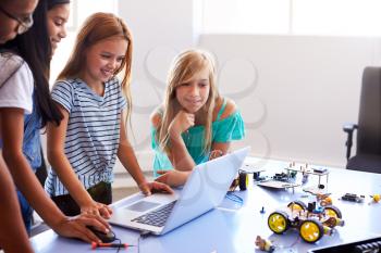 Three Female Students With Teacher Building Robot Vehicle In After School Computer Coding Class