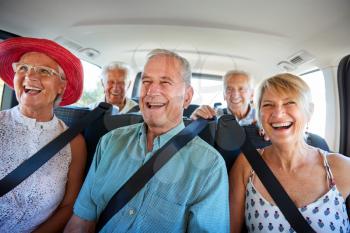 Group Of Senior Friends Sitting In Back Of Van Being Driven To Vacation