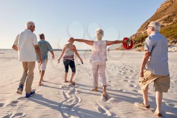 Rear View Of Senior Friends Walking Along Sandy Beach On Summer Group Vacation