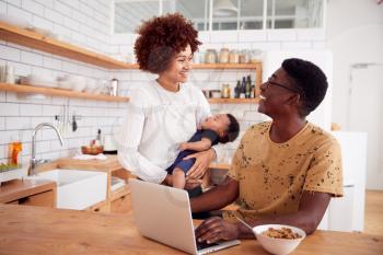 Busy Family In Kitchen At Breakfast With Father Caring For Baby Son