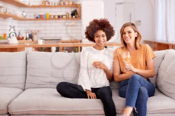 Portrait Of Two Female Friends Relaxing On Sofa At Home With Glass Of Wine Talking Together