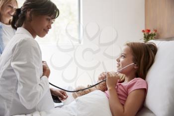 Female Doctor Letting Girl Patient Listen To Her Chest With Stethoscope In Hospital Bed
