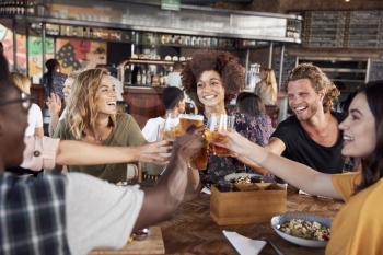 Group Of Young Friends Meeting For Drinks And Food Making A Toast In Restaurant