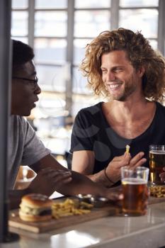 Two Male Friends Eating Food And Drinking Beer In Sports Bar
