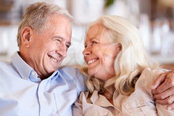 Happy senior white couple sit at home embracing, smiling at each other, head and shoulders, close up