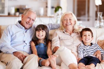 White senior couple and their grandchildren sitting on a sofa together at home smiling to camera