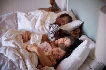 Mid adult parents and their two young children lying asleep in bed, waist up, close up