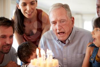 Senior white man celebrating with his family blowing out the candles on birthday cake, close up