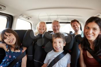 Three generation white family sitting in two rows of passenger seats in a car, smiling to camera