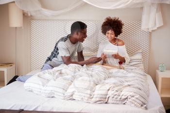 Millennial African American man giving his partner breakfast and gifts in bed to celebrate