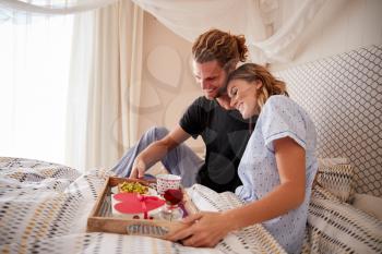 Millennial white couple embracing, after man serves breakfast and gifts in bed, close up