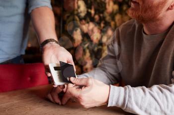 Close Up Of Customer Paying In Hotel Restaurant Using Contactless Card Reader