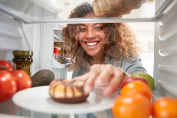 View Looking Out From Inside Of Refrigerator As Woman Opens Door And Reaches For Unhealthy Donut