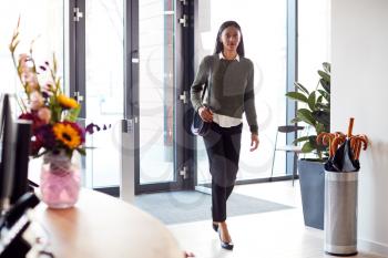 Businesswoman Arriving For Work At Office Walking Through Door