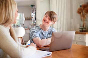 Downs Syndrome Man Sitting With Home Tutor Using Laptop For Lesson At Home