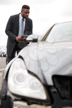 Male Insurance Loss Adjuster With Digital Tablet Inspecting Damage To Car From Motor Accident