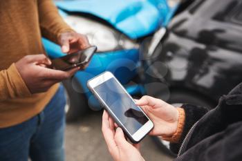 Close Up Of Two Motorists Swapping Insurance Details On Mobile Phone After Car Crash