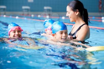 Female Coach In Water Giving Group Of Children Swimming Lesson In Indoor Pool
