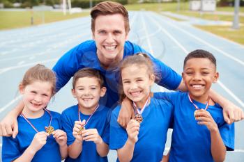 Portrait Of Children With Male Coach Showing Off Winners Medals On Sports Day