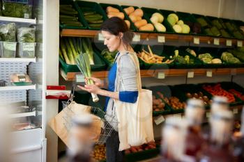 Female Customer With Shopping Basket Buying Fresh Leeks In Organic Farm Shop