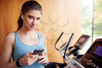 Portrait Of Woman Exercising Wearing Wireless Earphones And Smart Watch Checking Mobile Phone