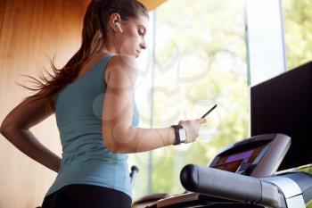 Woman Exercising On Treadmill Wearing Wireless Earphones And Smart Watch Checking Mobile Phone
