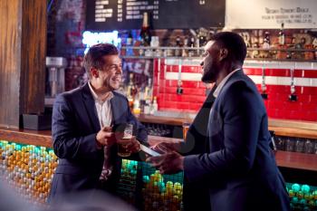 Two Businessmen Meeting For Drinks And Socializing In Bar After Work