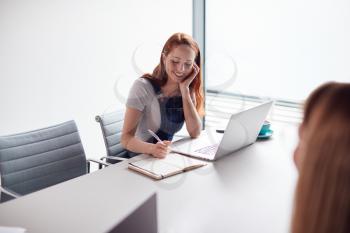 Two Casually Dressed Young Businesswomen Working On Laptops In Modern Meeting Room