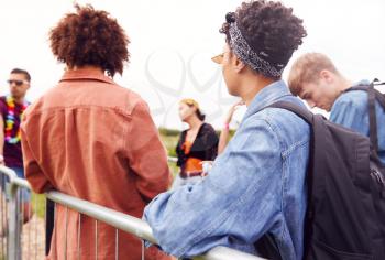 Group Of Young Friends Waiting Behind Barrier At Entrance To Music Festival Site