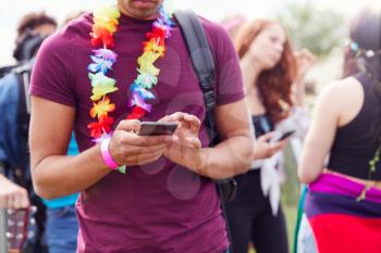 Close Up Of Man Looking At Mobile Phone As He Waits Behind Barrier At Entrance To Music Festival