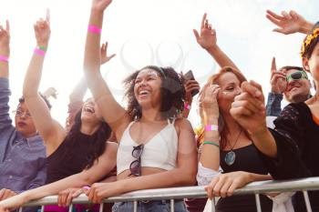 Young Friends In Audience Behind Barrier Dancing And Singing At Outdoor Festival Enjoying Music