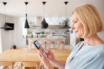 Mature Woman Using App On Digital Tablet To Control Central Heating Temperature In House