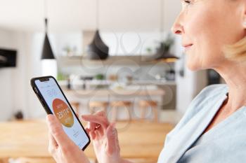 Mature Woman Using App On Digital Tablet To Control Central Heating Temperature In House