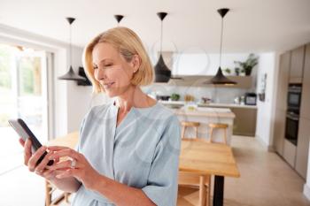 Mature Woman Using App On Mobile Phone To Control Central Heating Temperature In House