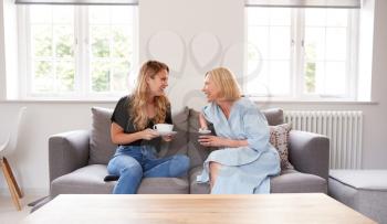 Senior Mother With Adult Daughter Sitting On Sofa Indoors Drinking Coffee And Talking
