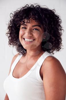Portrait Of Smiling Casually Dressed Woman In Vest Top Standing Against White Brick Studio Wall