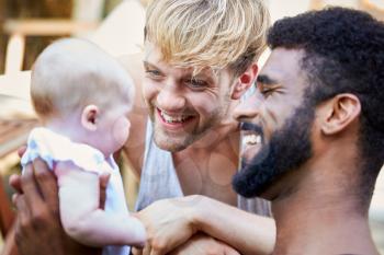 Loving Male Same Sex Couple Cuddling Baby Daughter At Home In Garden Together