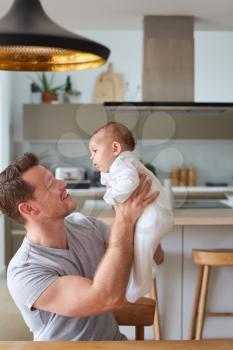 Loving Father Holding 3 Month Old Baby Daughter In Kitchen At Home