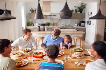 Multi-Generation Mixed Race Family Eating Meal Around Table At Home Together