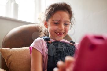 Girl Sitting In Armchair At Home Playing With Digital Tablet