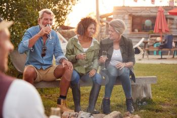 Group Of Mature Friends Sitting Around Fire And Drinking At Outdoor Campsite Bar