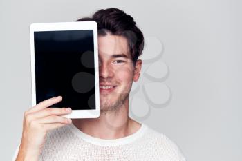 Studio Portrait Of Smiling Young Man Covering Face With Digital Tablet