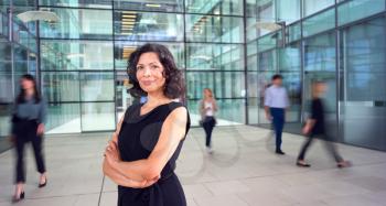 Portrait Of Mature Businesswoman With Crossed Arms Standing In Lobby Of Busy Modern Office