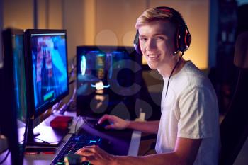 Portrait Of Teenage Boy Wearing Headset Gaming At Home Using Dual Computer Screens