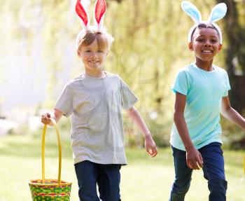 Group Of Children Wearing Bunny Ears Running On Easter Egg Hunt In Garden