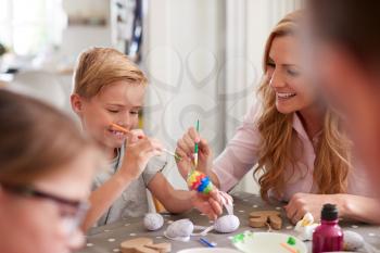 Parents With Children Sitting At Table Decorating Eggs For Easter At Home