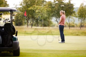 Rear View Of Woman Getting Out Of Golf Buggy To Play Shot On Green